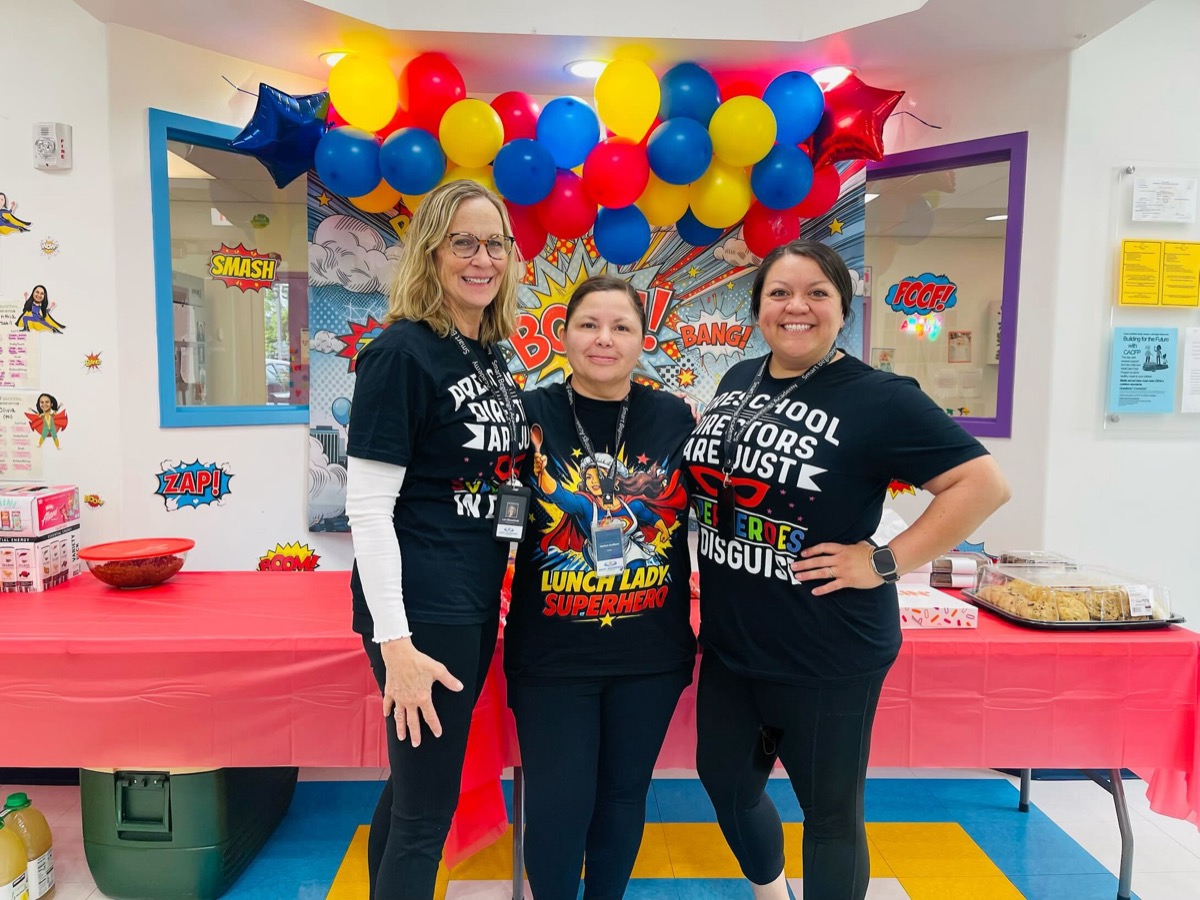 Three team members in superhero shirts, smiling together